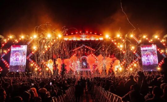 imagem mostra palco da festa do pinhão iluminado com público massivo, luzes e confetes