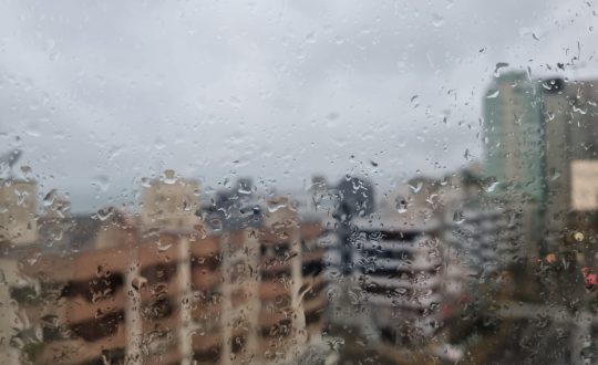 Imagem mostra a visão de prédios com pingos na janela