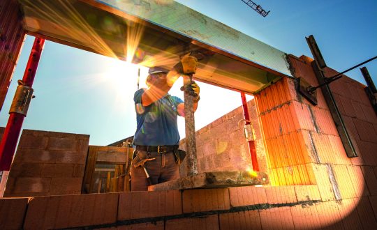 Imagem mostra pedreiro firmando uma viga de concreto em uma construção