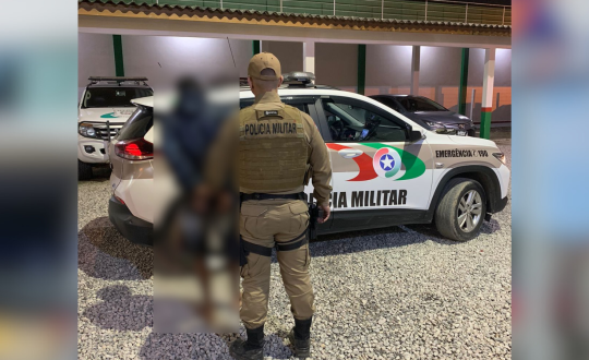 Imagem mostra homem em frente a viatura