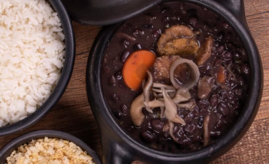 Feijoada vegana no bowl preto e bowl com arroz e farofa ao lado