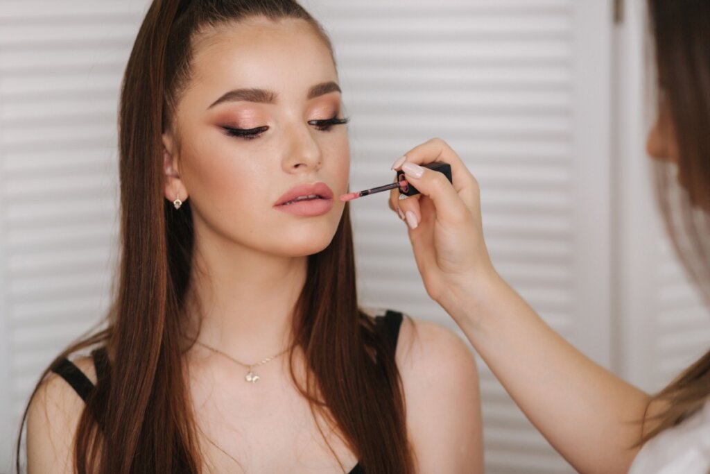 Mulher com olhos fechados e uma mão passando batom em sua boca 