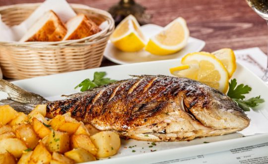 Peixe em cima de um prato branco com batatas e rodelas de laranja