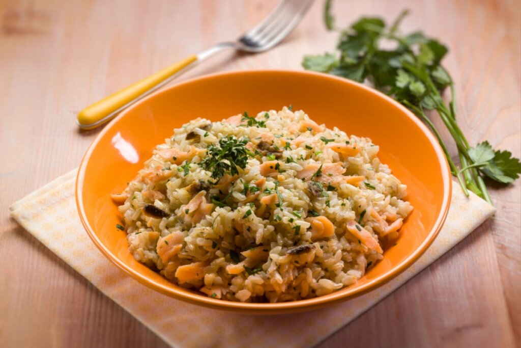 Risoto de salmão servido em prato fundo de cerâmica laranja 