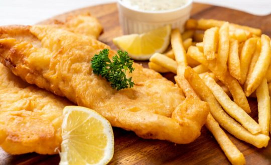 Peixe frito em cima de uma tábua com batatas fritas