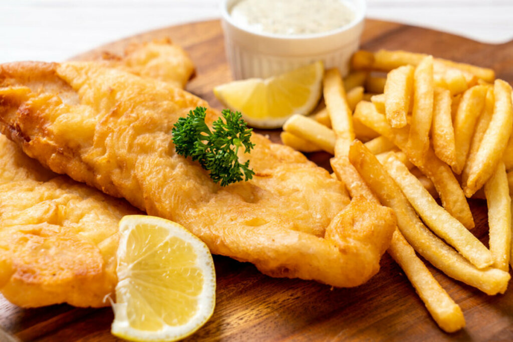 Peixe frito em cima de uma tábua com batatas fritas 