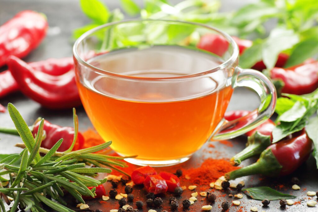 Chá de pimenta com ervas em xícara de vidro com pimentas e ervas ao redor
