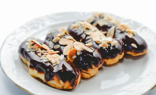 Quatro éclairs com cobertura de chocolate e amêndoas em prato branco