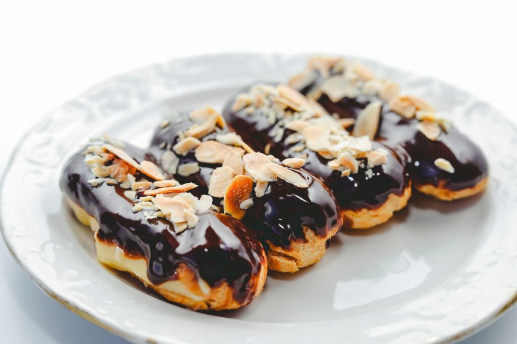Quatro éclairs com cobertura de chocolate e amêndoas em prato branco