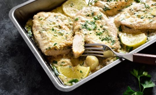 Assadeira com frango, molho, dentes de alho e rodelas de limão