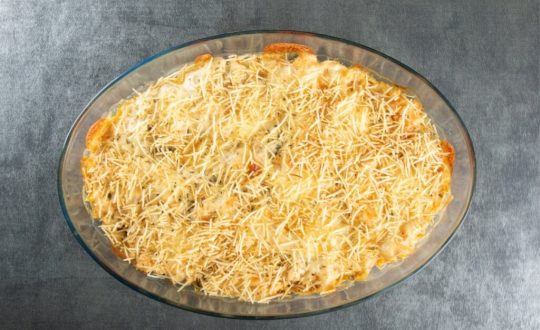 Travessa de vidro com fricassê polvilhado com batata-palha em cima de uma mesa cinza