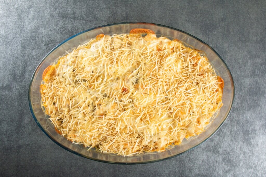 Travessa de vidro com fricassê polvilhado com batata-palha em cima de uma mesa cinza 