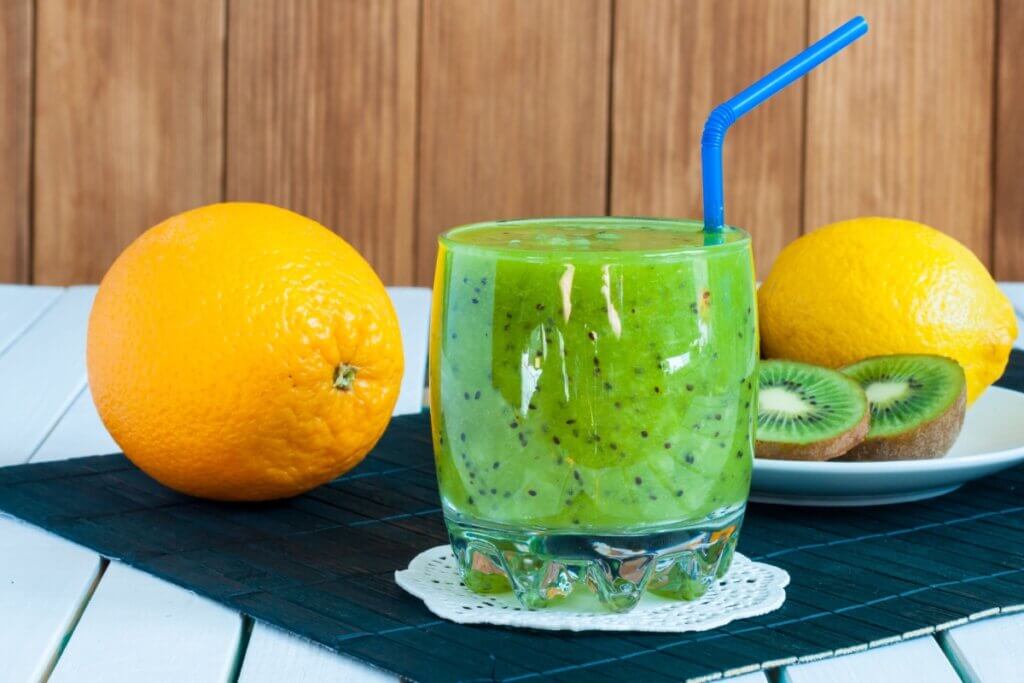 Suco de kiwi, limão-siciliano e laranja em copo; laranja, kiwi e limão perto do copo