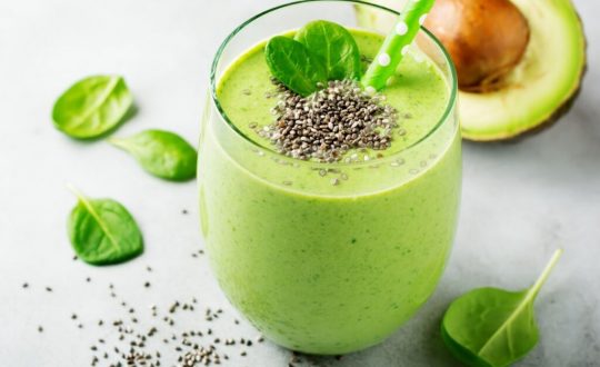 Copo de vidro com vitamina de abacate decorado com folhas de espinafre e sementes de chia