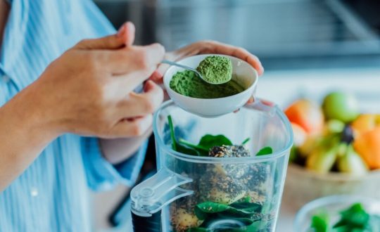 Mãos colocando pó verde em um liquidificador