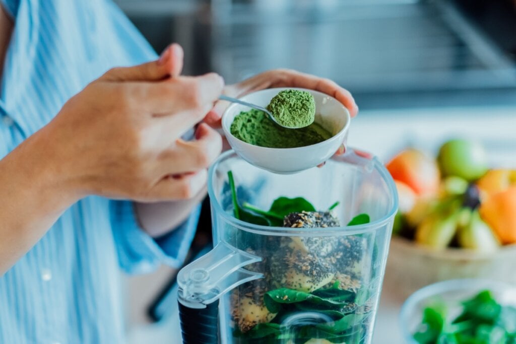 Mãos colocando pó verde em um liquidificador 