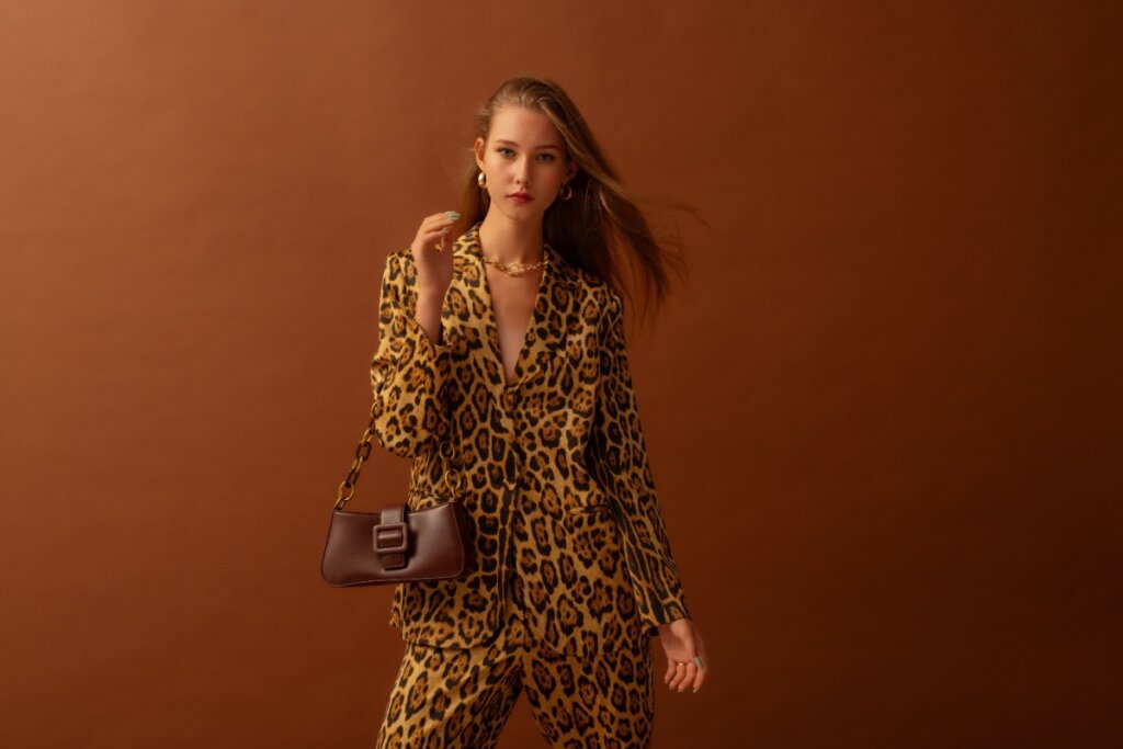 Modelo segurando bolsa e vestindo conjunto de animal print em fundo marrom