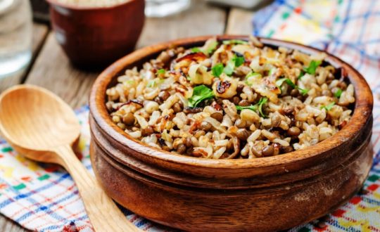 Arroz com lentilha e cebola servido em tigela de madeira em cima de mesa de madeira