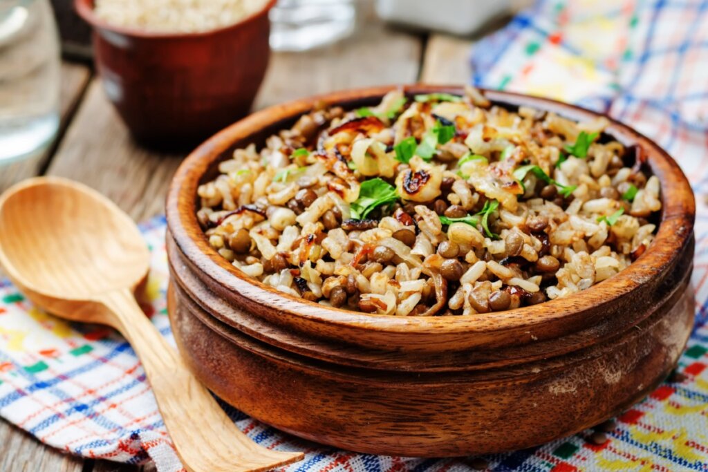 Arroz com lentilha e cebola servido em tigela de madeira em cima de mesa de madeira