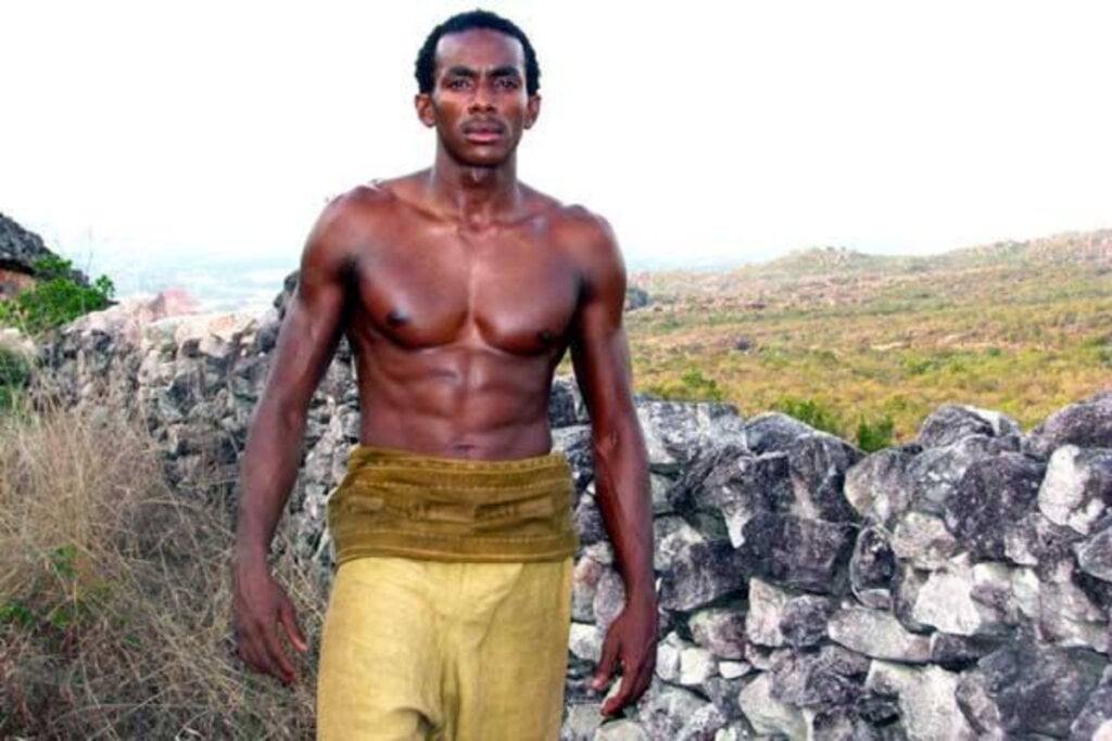 Cena do filme "Besouro" com homem negro sem camisa e calça amarela
