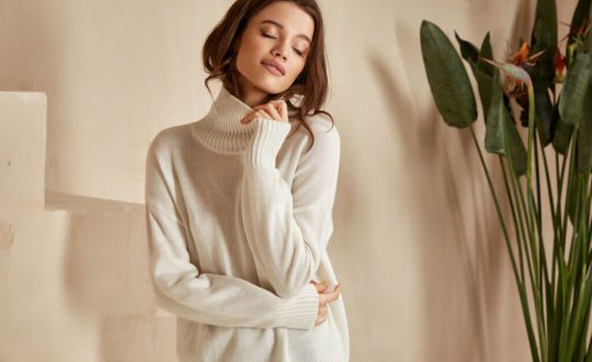 Mulher com olhos fechados e cabeça para o lado vestindo blusa de tricot