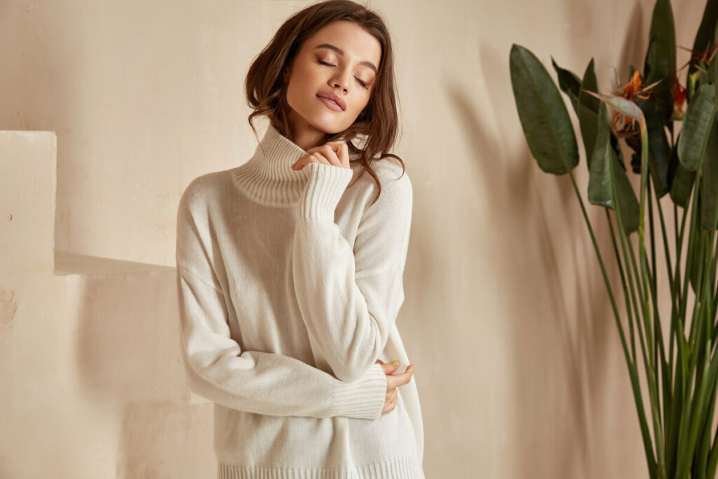 Mulher com olhos fechados e cabeça para o lado vestindo blusa de tricot