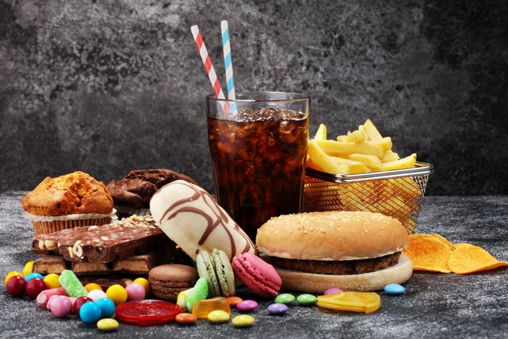 Alimentos processados e ricos em açúcar e gordura em cima de mesa de pedra como hambúrguer, refrigerante, chocolate e batata frita