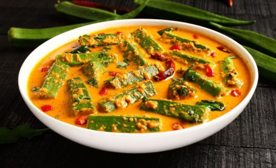 Curry de quiabo servido em tigela grande branca de porcelana em cima de mesa de madeira