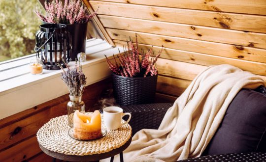 Ambiente com poltrona preta, manta bege, mesa com vela, chá e plantas