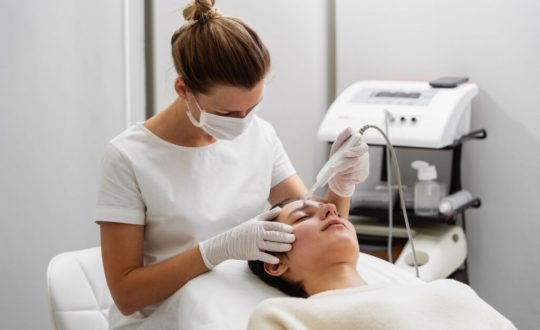 Mulher fazendo procedimento estético em uma mulher deitada com olhos fechados