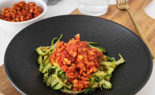 Espaguete de abobrinha com proteína de soja e molho de tomate em prato preto