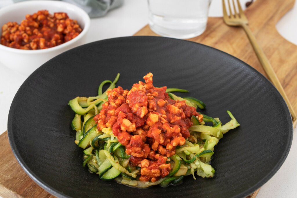 Espaguete de abobrinha com proteína de soja e molho de tomate em prato preto