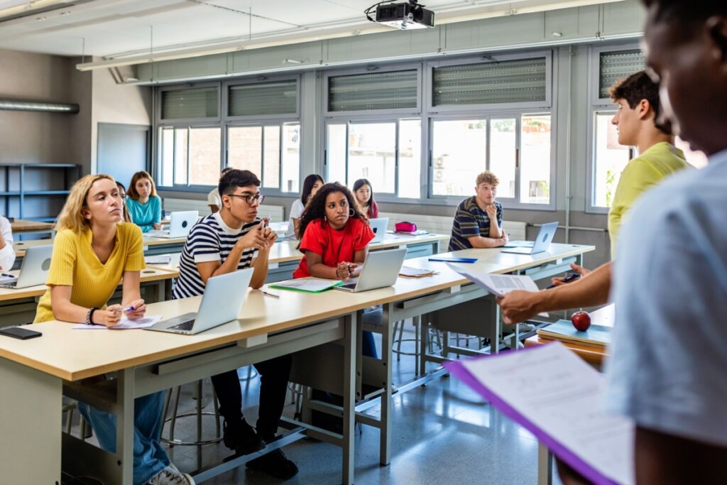 Alunos sentados em mesas na sala de aula assistindo apresentação de projeto de um colega que está a frente da sala