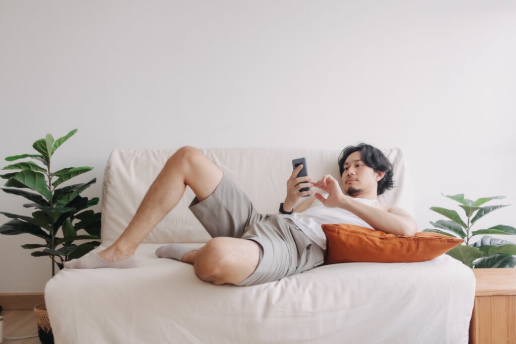 Homem deitado em um sofá mexendo em um celular 