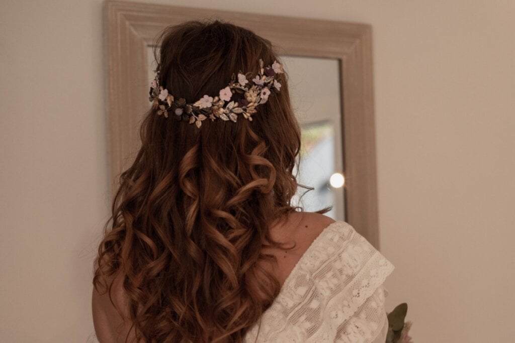 Mulher vestida de noiva com o cabelo preso na parte de cima com um arranjo floral, com o cabelo castanho e cacheado