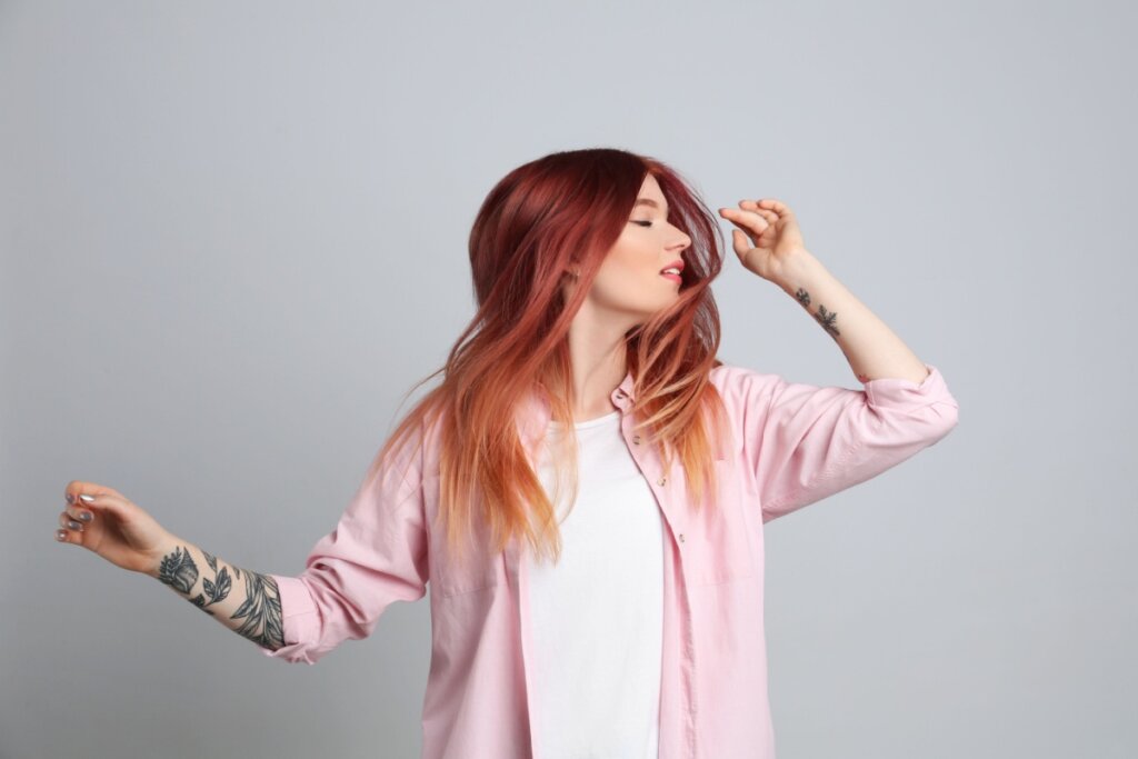 mulher de camiseta branca e camisa rosa balançando o cabelo ruivo rosado