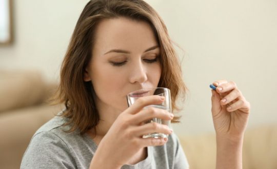 Mulher tomando comprimido com um copo de água