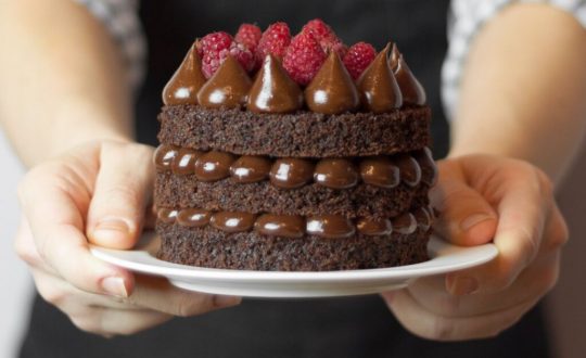 Mãos segurando um naked cake de chocolate com morangos