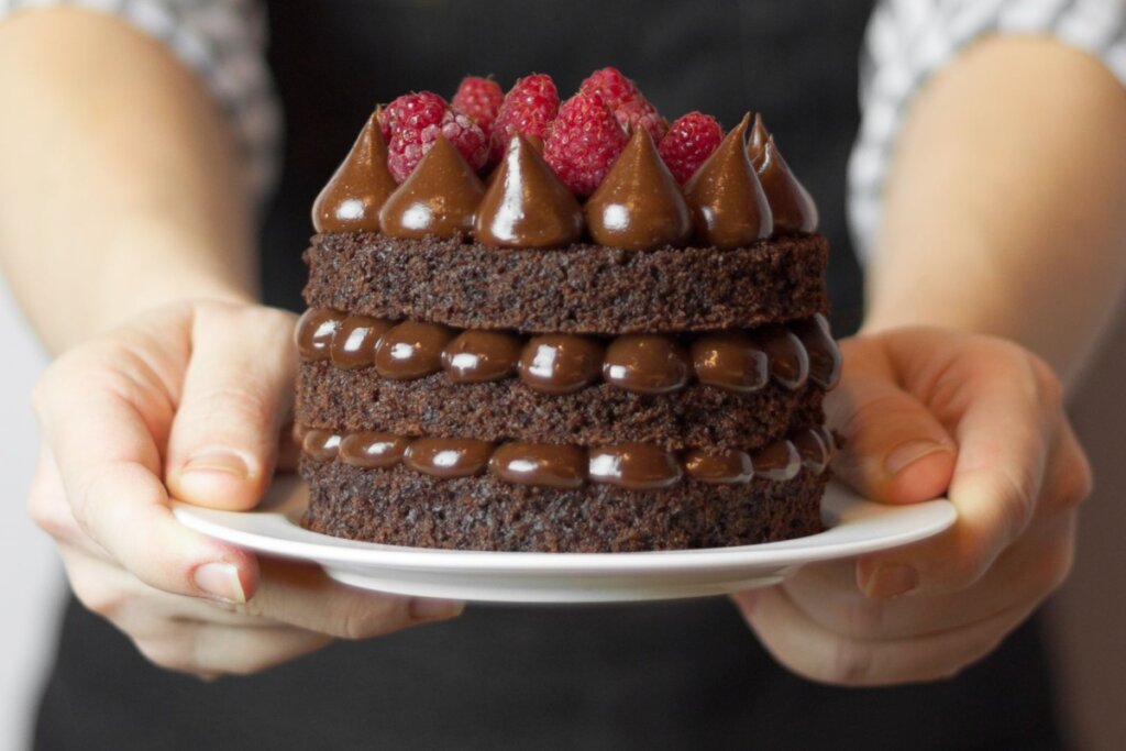 Mãos segurando um naked cake de chocolate com morangos 