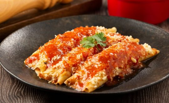 Panqueca de carne moída servida em prato de cerâmica preto em cima de mesa de madeira