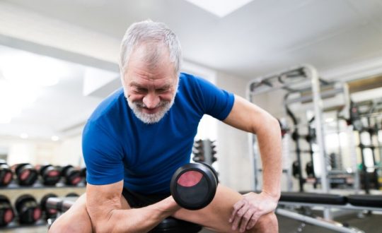 Homem sentado e levando peso com o braço em uma academia