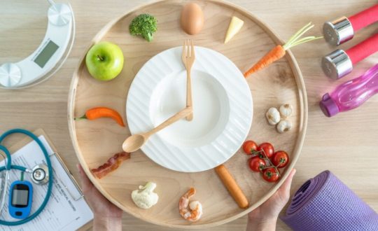 prato com talheres imitando um relógio e alimentos saudáveis em volta, como ovo, maçã, tomate etc.