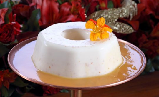 Pudim de coco com calda de caramelo e decorado com flores.