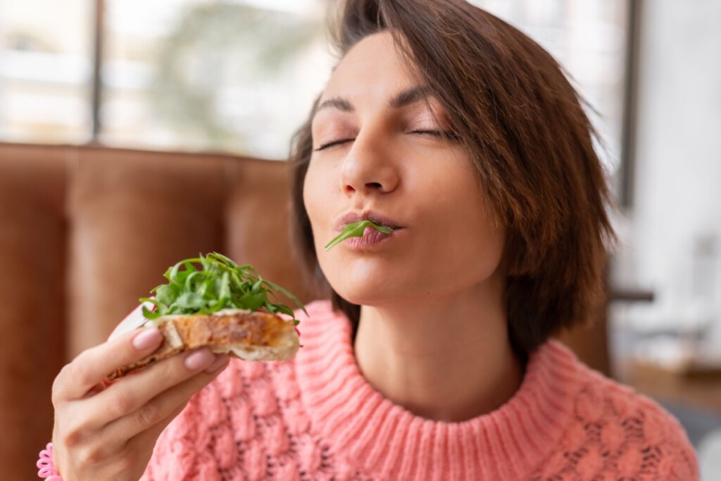 Mulher comendo torrada com rúcula e com os olhos fechados 