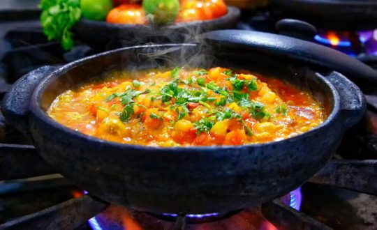 Moqueca na panela preta em cima do fogão com cebolinha