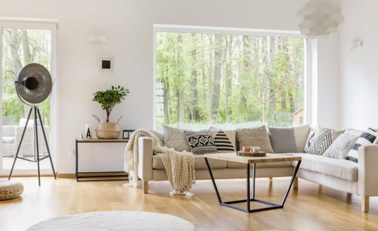 Sala de estar com janela ao fundo, sofá branco e mesa de centro de madeira