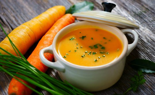 Panela de vidro branca com sopa de cenoura polvilhada com salsinha