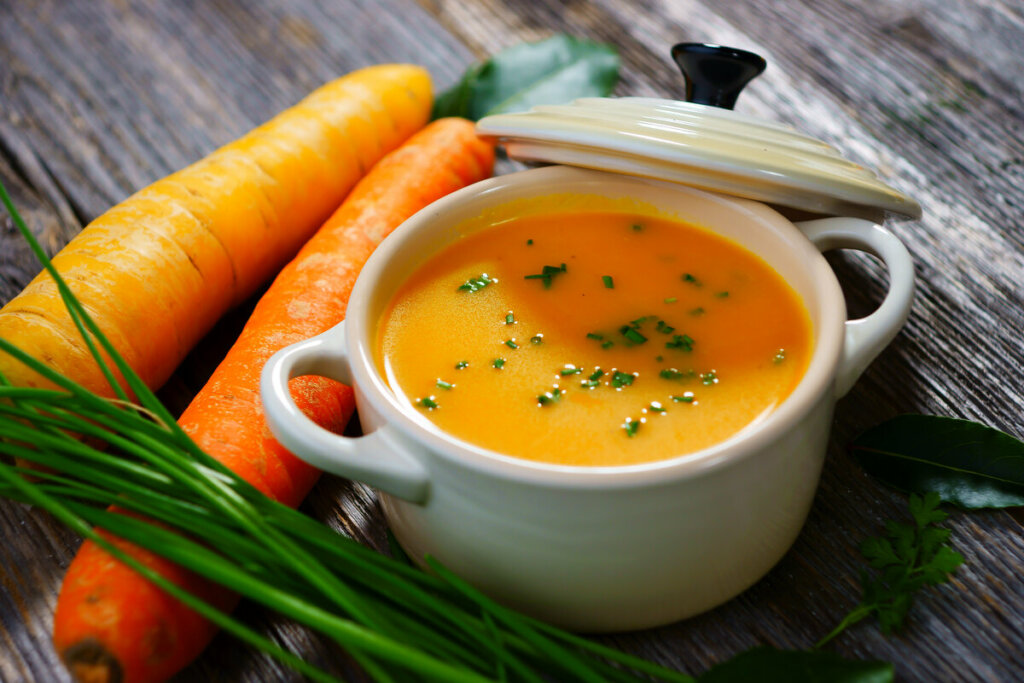 Panela de vidro branca com sopa de cenoura polvilhada com salsinha