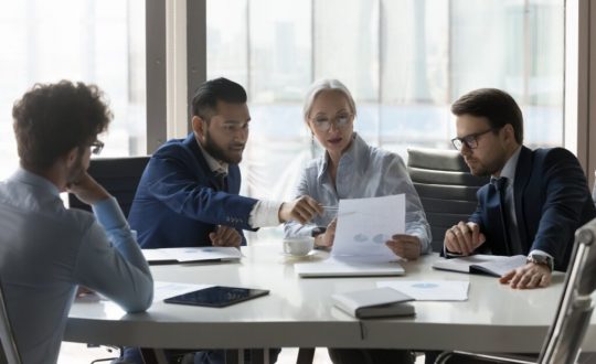 Profissionais de uma empresa conversando e analisando papéis em conjunto sentados à mesa