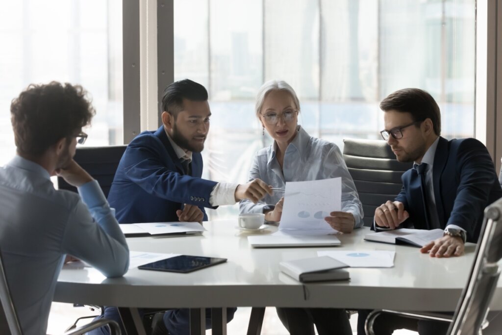 Profissionais de uma empresa conversando e analisando papéis em conjunto sentados à mesa